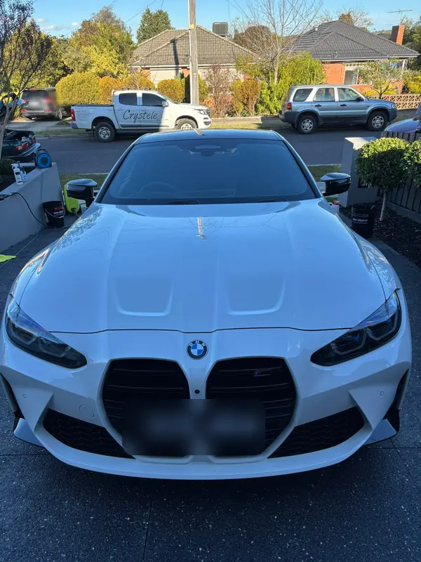 Front of the white BMW M4 on a driveway, bonnet and grille after the detail